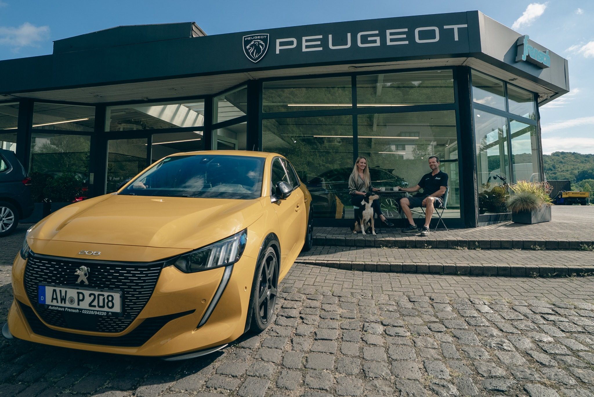 Jeanette und Florian Frensch mit Hund vor dem Autohaus Frensch in Remagen-Oberwinter, davor ein gelber Peugeot 208