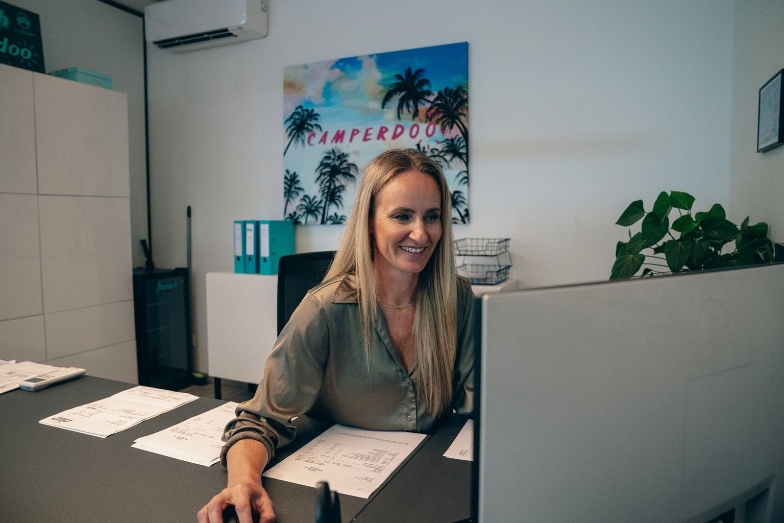 Jeanette Frensch im Camperdoo-Büro am Schreibtisch, an der Wand ein Camperdoo-Bild mit Palmen